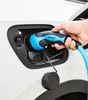 A hand is holding a blue and black electric car charging plug, inserting it into the charging port of a white car. Náhľad obrázku produktu