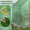A green greenhouse with plants inside, showing how to secure it with stones and ground anchors. Podgląd zdjęcia produktu