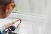 A person is using a caulking gun to apply sealant around a window frame. Produktbild-Vorschau
