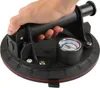 A hand is holding a black suction cup lifter with a pressure gauge. Produktbild-Vorschau