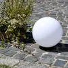 A white spherical lamp sits on a cobblestone patio next to a planter with greenery. Produktbild-Vorschau