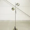 A floor lamp with two circular shades stands against a white wall with horizontal lines. Produktbild-Vorschau