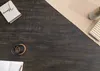 A dark wooden table with a notebook, a cup of coffee, and a vase with a book on a piece of brown paper. Produktbild-Vorschau