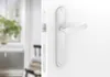A close-up view of a white door handle and lock mechanism, with a blurred background of a room. Produktbild-Vorschau