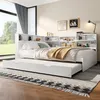 A white daybed with a pull-out trundle bed, set up in a bedroom with a large window and decorative items on the headboard shelves. Produktbild-Vorschau