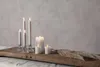 A collection of LED candles of various sizes and styles are arranged on a rustic wooden plank, with dried grass plumes to the right, against a textured gray background. Podgląd zdjęcia produktu