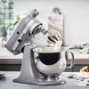 A KitchenAid stand mixer is shown in a kitchen setting, actively mixing ingredients in a bowl. Podgląd zdjęcia produktu