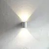 A white cylindrical wall lamp mounted on a textured white wall, casting light upwards and downwards. Produktbild-Vorschau