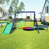 A backyard playground set with a swing, slide, and trampoline, set in a grassy yard with houses in the background. Produktbild-Vorschau