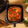 A square pizza with basil leaves is in an air fryer basket, placed on a wooden table. Produktbild-Vorschau