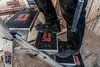 A person wearing work boots and dark pants is standing on a Little Giant ladder with three steps. The ladder is in a construction environment with wooden planks in the background. Anteprima dell’immagine prodotto