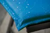 Close-up of a blue cushion with water droplets on it, resting on a black metal frame. Produktbild-Vorschau