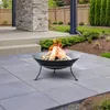 A fire pit with burning logs on a paved patio, with a stone-clad pillar and garden in the background. Produktbild-Vorschau
