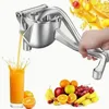 A hand is shown using a manual juicer to extract juice from fruit. A glass of orange juice is being filled, and various fruits are arranged at the bottom right of the image. Produktbild-Vorschau