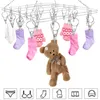 A stainless steel sock dryer with clips, holding various baby clothes and a teddy bear, against a white background. Produktbild-Vorschau