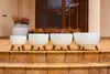 Four white planters with wooden legs are arranged on a tiled porch. Náhled obrázku produktu