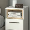 A white bedside table with a drawer and an open shelf containing books. A digital clock is on top of the table. Náhled obrázku produktu