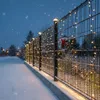 A snowy fence decorated with Christmas lights and a wreath. Voir les images du produit