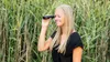 A woman is looking through binoculars in a field of tall grass. Produktbild-Vorschau