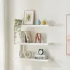 Three white shelves mounted on a white wall, displaying various decorative items and books. Produktbild-Vorschau