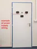 A white door with several electronic devices mounted on it, with a red line indicating power supply wiring. Produktbild-Vorschau