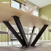 A close-up view of a wooden table with a black metal V-frame base, set in a modern dining room with chairs and a green wall. Voir les images du produit