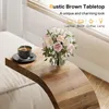 A C-shaped side table with a cup of coffee and a vase of flowers on it, placed next to a sofa. Anteprima dell’immagine prodotto