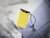 A yellow power bank with a black display and a black lanyard is placed on a blue surface with a blurred background. Voir les images du produit
