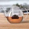 A glass teapot filled with tea and tea leaves, placed on a wooden table. Produktbild-Vorschau