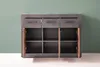 A gray sideboard with three drawers and three open cabinets against a green wall. Produktbild-Vorschau