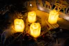 Four LED candles are arranged on a rustic surface with decorative elements, suggesting a festive or cozy atmosphere. Náhľad obrázku produktu