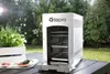 A Tepro gas grill is shown outdoors on a table, with greenery and ingredients in the foreground. Produktbild-Vorschau