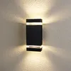 A black rectangular outdoor wall light mounted on a textured wall, emitting light upwards and downwards. Produktbild-Vorschau