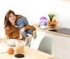 A mother is holding her child in a kitchen setting, with a humidifier on the counter. Voir les images du produit