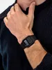 A person wearing a black striped shirt and a black calculator watch. Produktbild-Vorschau