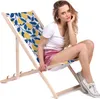 A woman is sitting on a foldable deck chair with a tropical lemon pattern. Produktbild-Vorschau