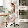 A woman is sitting on a pink ergonomic meditation chair at a desk with a computer. Produktbild-Vorschau