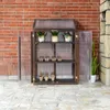 A mini greenhouse with plants on shelves, set against a brick wall. Voir les images du produit