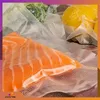 A close-up view of vacuum-sealed food items, including a piece of salmon, broccoli, and a lemon. Podgląd zdjęcia produktu