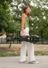 A woman is walking outdoors, carrying a folded stroller. Produktbild-Vorschau