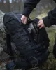 A person is putting a water bottle into a black backpack in a forest setting. Produktbild-Vorschau