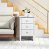 A white nightstand with three drawers sits next to a sofa, with stairs in the background. Produktbild-Vorschau