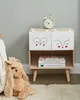 A child's bedside table with drawers decorated with animal faces, a stuffed bunny, and books. Náhled obrázku produktu
