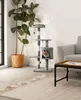 A cat tree with a cat inside, next to a large potted plant and a sofa. Produktbild-Vorschau