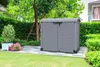 A grey plastic storage box is shown in a garden setting, placed on a paved patio area. Náhled obrázku produktu