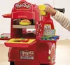 A child's hand is shown interacting with a red Play-Doh pizza delivery scooter set, which includes various Play-Doh accessories and a simulated screen. Produktbild-Vorschau