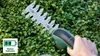 A hand holding a green and black Bosch hedge trimmer, trimming a dense green hedge. Anteprima dell’immagine prodotto