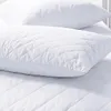 Two white quilted pillows are stacked on top of each other, with the bottom pillow resting on a quilted surface. Produktbild-Vorschau