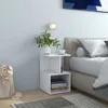 A bedside table with books and a vase of plants next to a bed. Náhled obrázku produktu