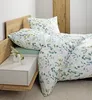A neatly made bed with floral patterned bedding, a wooden headboard, and a bedside table with vases. Produktbild-Vorschau